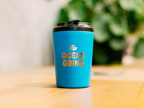 Bondi Fressko cup with 'Ocean Grind' logo on a blurred natural background
