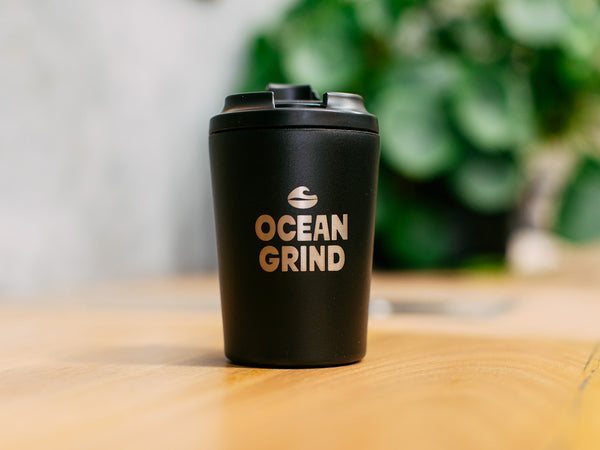 Coal Fressko cup with 'Ocean Grind' logo on a blurred natural background